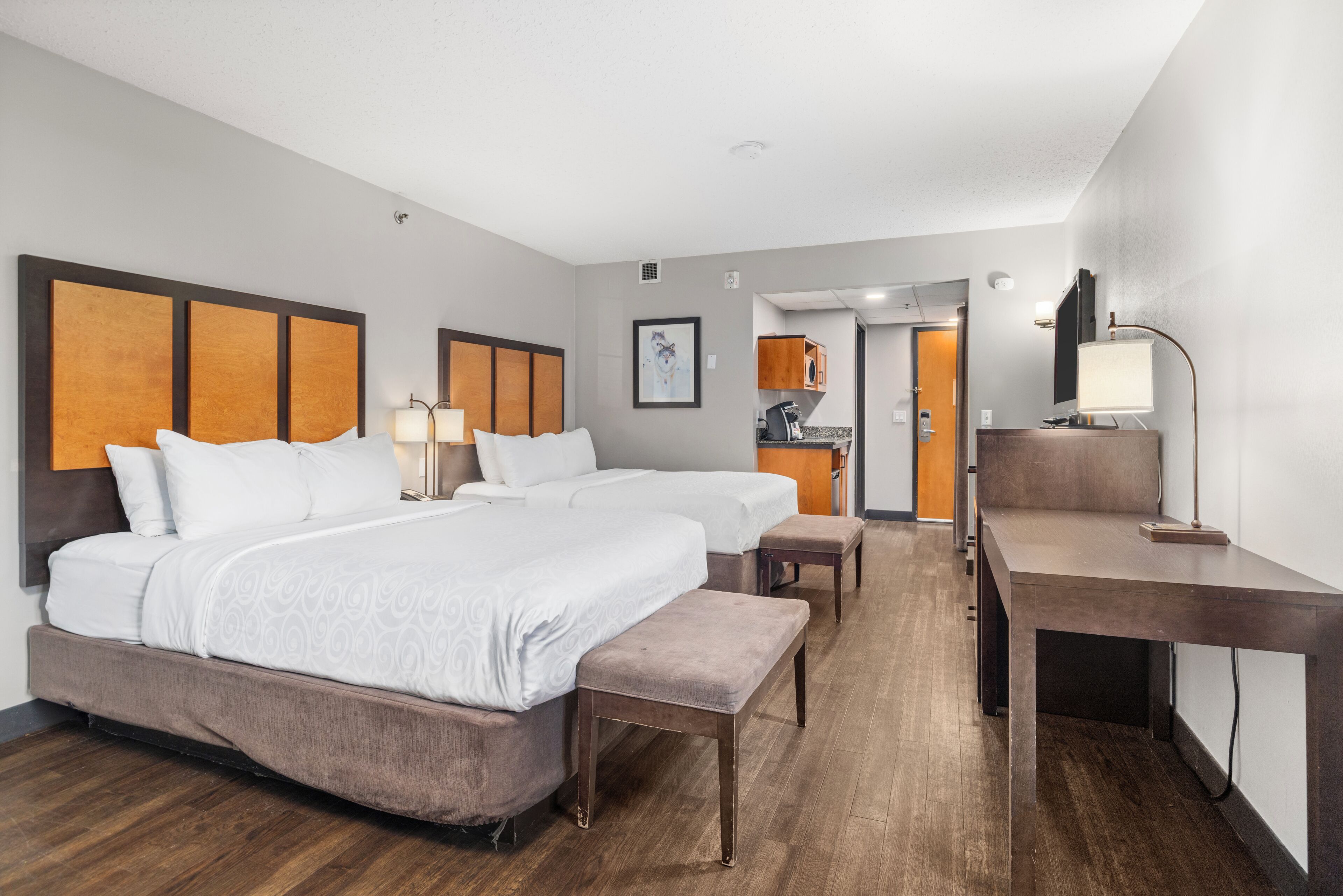 A hotel room with two beds, a desk, a chair, a small table, and a kitchenette area.