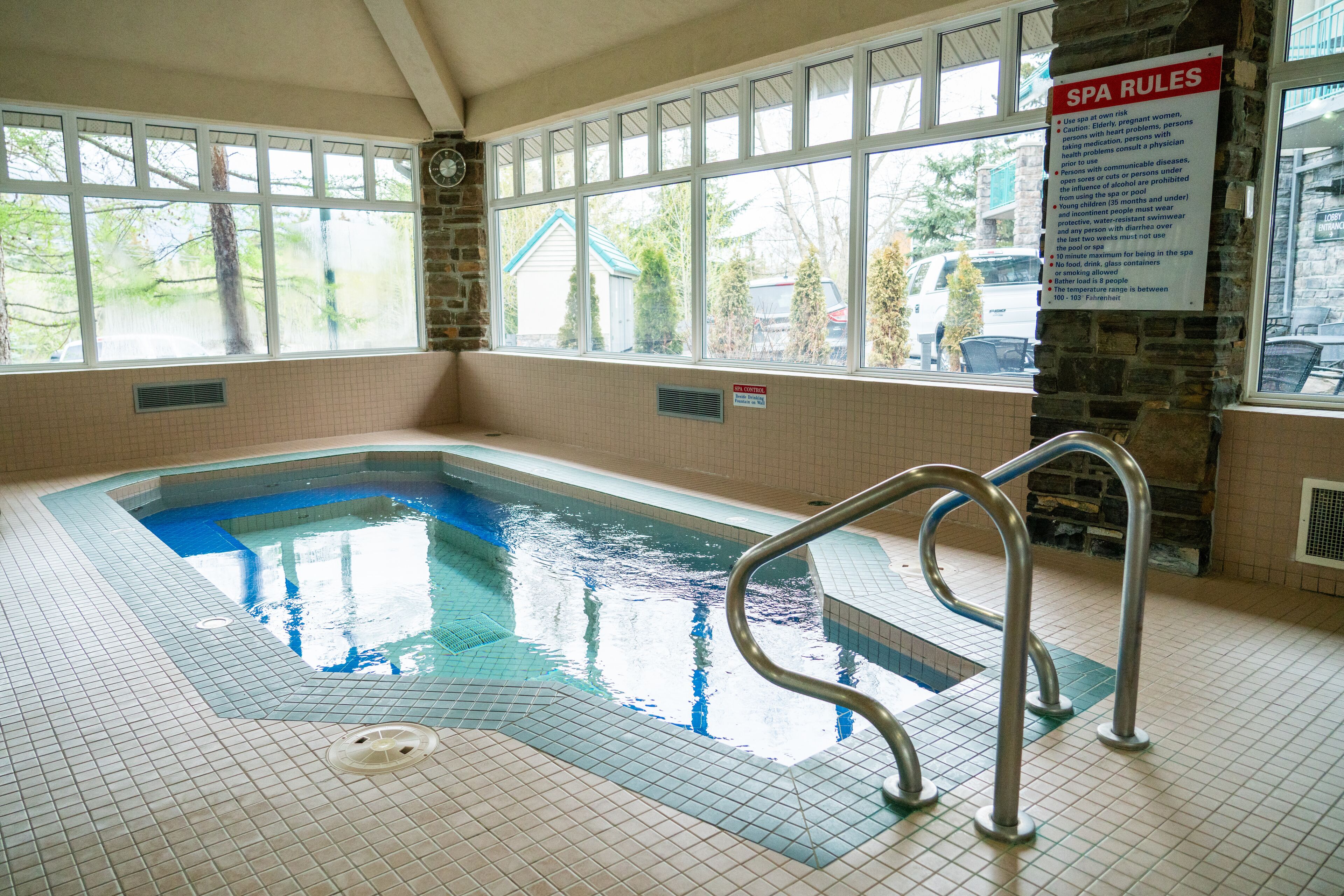 Une piscine intérieure offrant une vue dégagée sur le panneau indiquant les règles du spa, un mur en pierre et une fenêtre donnant sur l’extérieur.