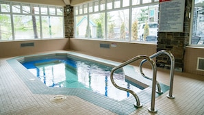 An indoor swimming pool with a clear view of the spa rules sign, a stone wall, and a window overlooking the outside. - Pocaterra Inn and Waterslide (Canmore)