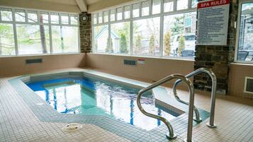 Une piscine intérieure offrant une vue dégagée sur le panneau indiquant les règles du spa, un mur en pierre et une fenêtre donnant sur l’extérieur.
