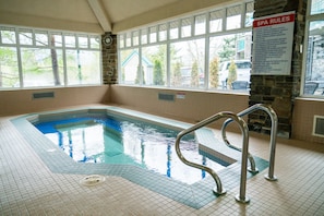 Una piscina interior con vista a un cartel de normas del spa, una pared de piedra y una ventana que da al exterior.