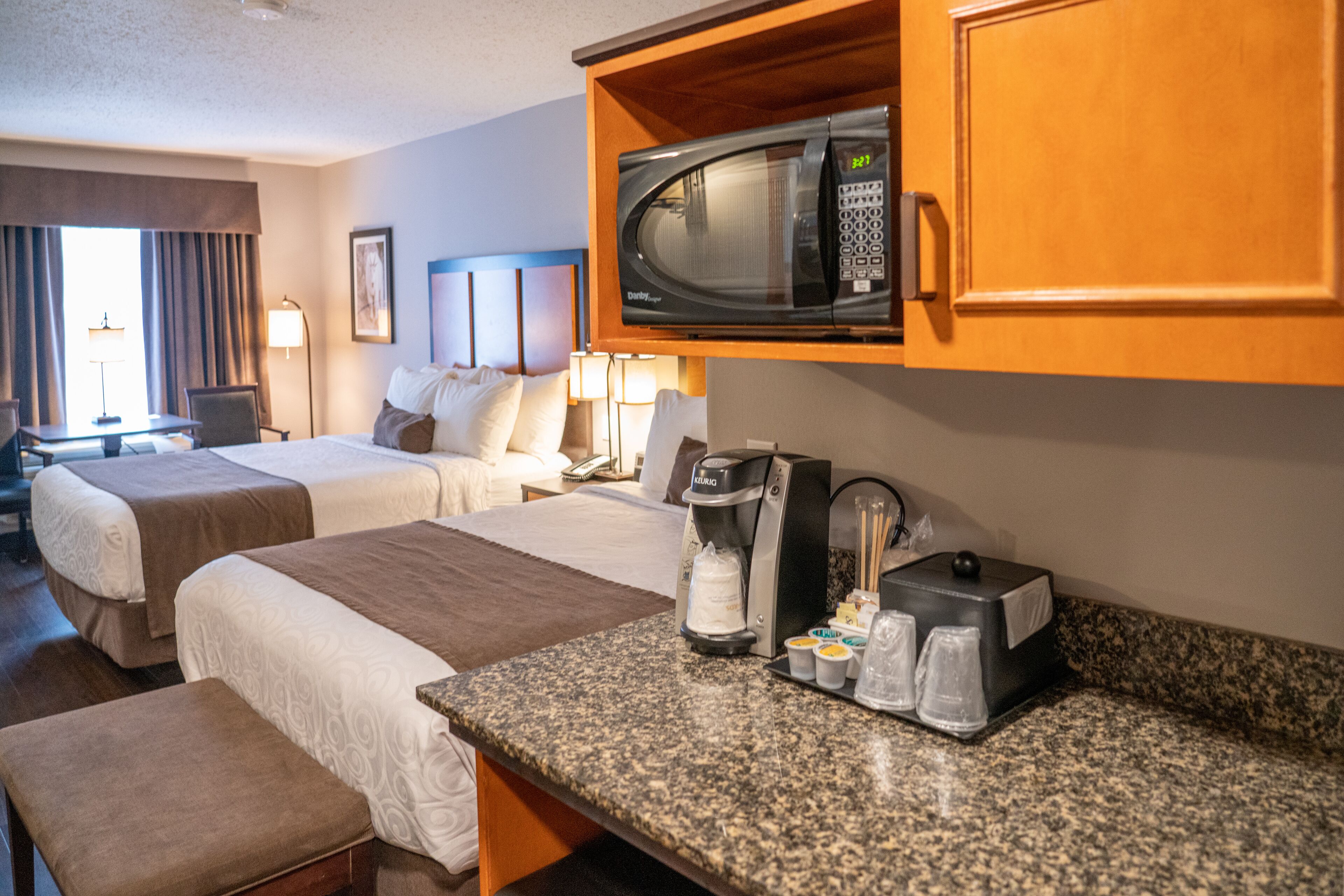 Habitación de hotel con dos camas, kitchenette, microondas, cafetera y una mesita con tazas y bandeja.