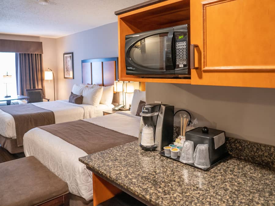 Habitación de hotel con dos camas, kitchenette, microondas, cafetera y una mesita con tazas y bandeja.
