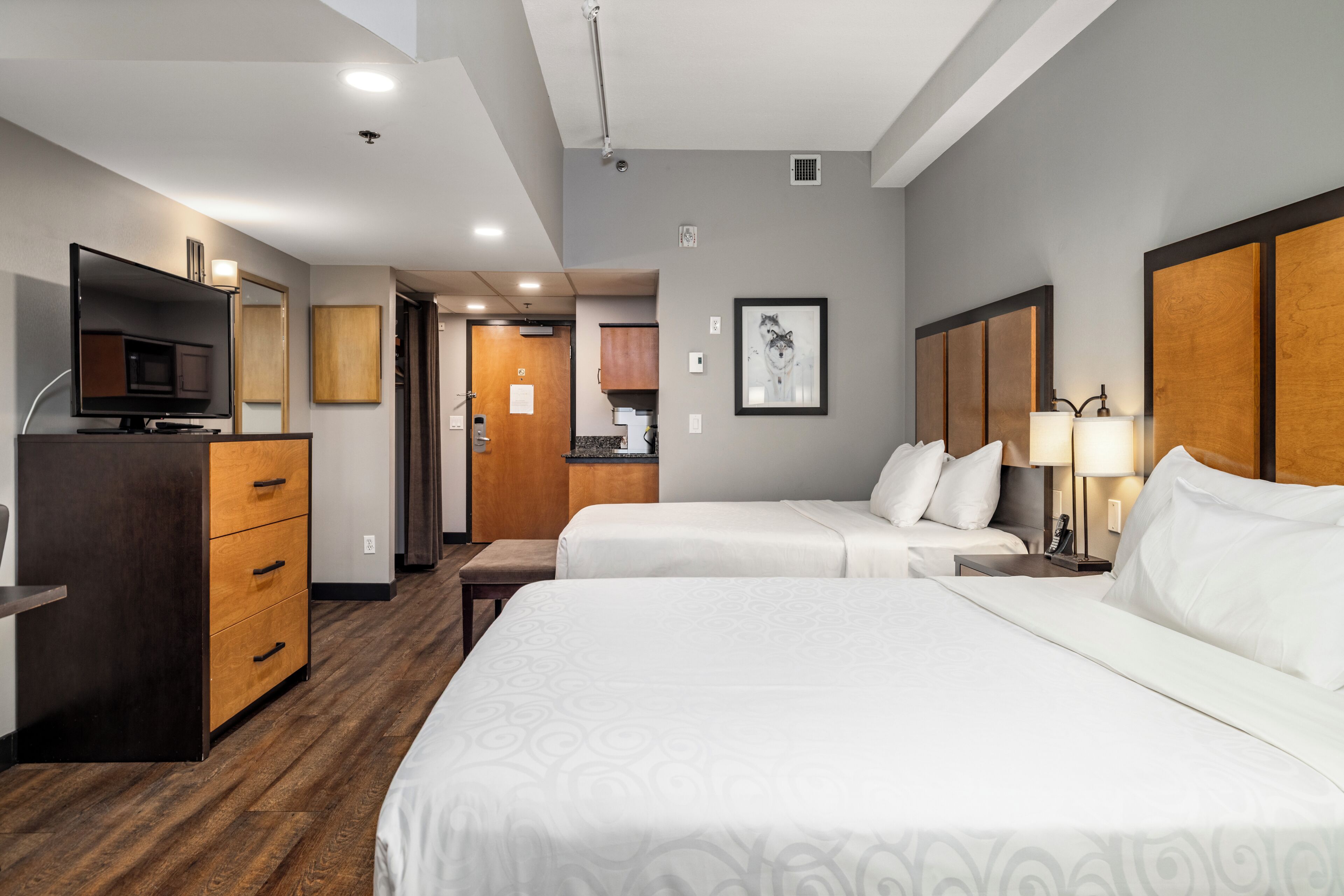 A hotel room with two beds, a television, a desk, and a kitchenette.