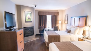 A hotel room with a TV, fireplace, two beds, a desk, and a window with curtains. - Pocaterra Inn and Waterslide (Canmore)