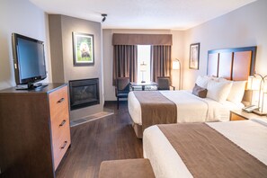 Habitación de hotel con televisión, chimenea, dos camas, escritorio y ventana con cortinas.