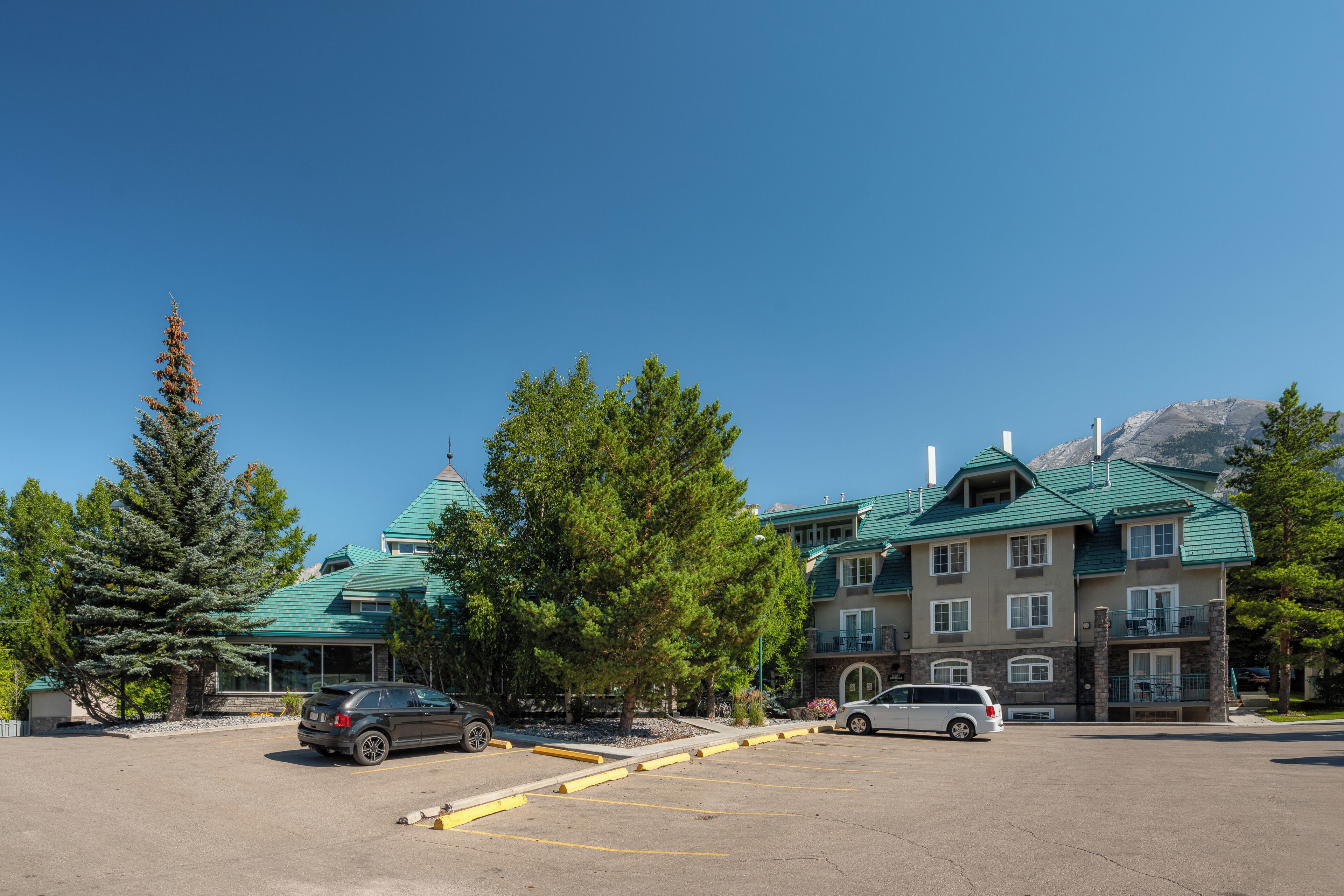 A multi-story building with a green roof, surrounded by trees and a parking lot with two cars.