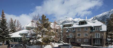 A multi-story hotel with a snow-covered roof, parking lot, and mountains in the background.