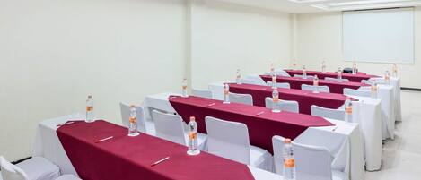 A conference room with rows of tables covered in red tablecloths, white chairs, and water bottles.