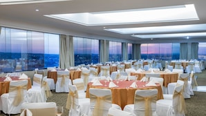 Un salón de banquetes con mesas redondas, sillas y vistas a la ciudad.