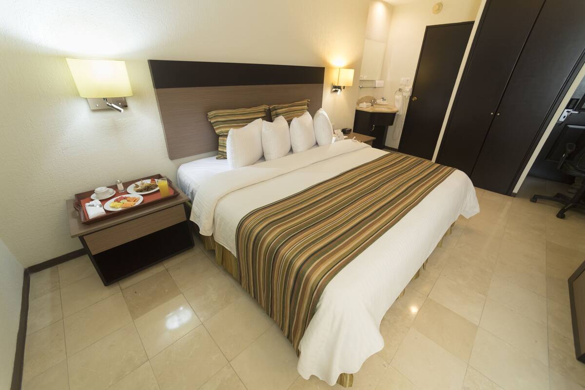 Habitación de hotel con cama, mesita de noche con una bandeja de desayuno, mesita de noche con lámpara y armario.