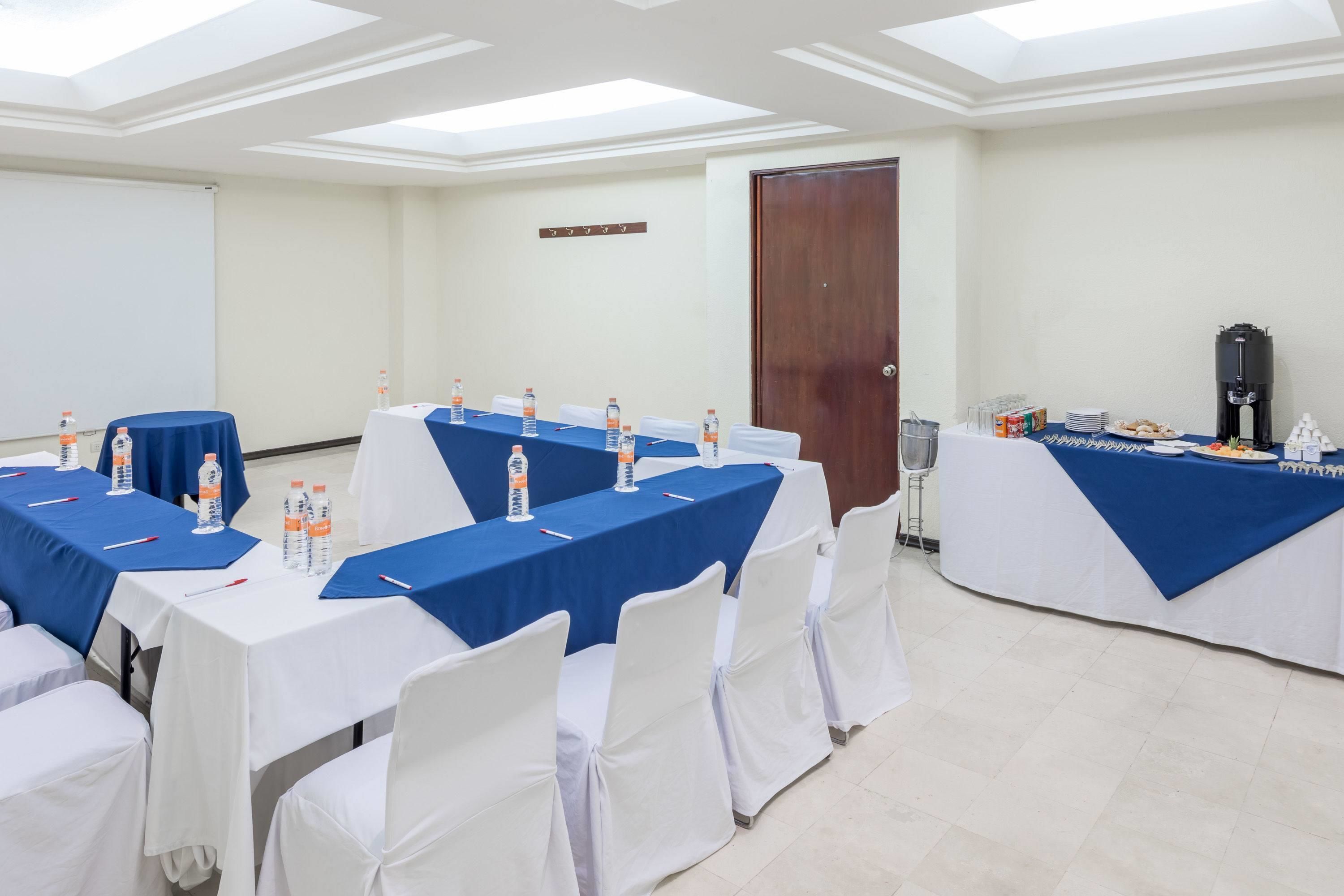 A conference room with tables set for a meeting, equipped with water bottles and pens, and a coffee station.