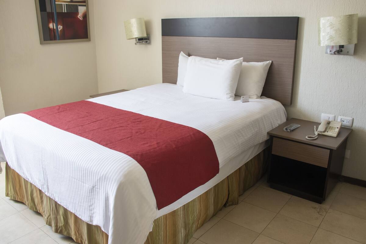 Una habitación de hotel con una cama grande, una mesita de noche con un teléfono y una lámpara de pared.