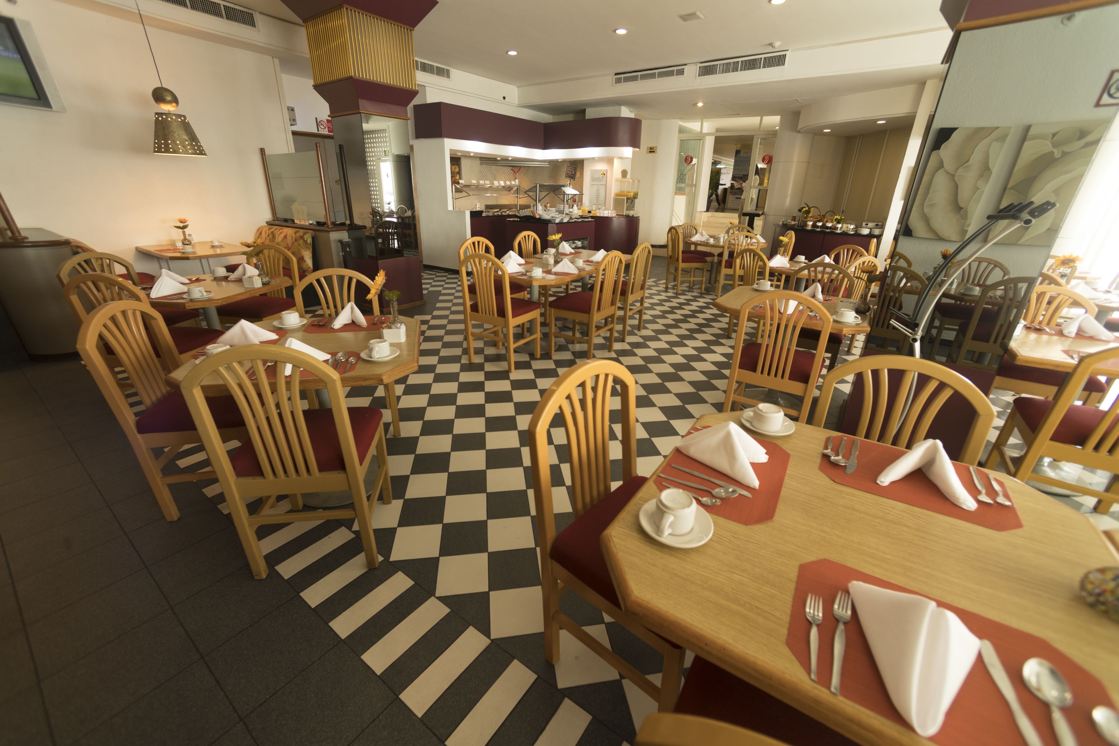 A restaurant with checkered flooring, wooden chairs, and tables set with white napkins and silverware.