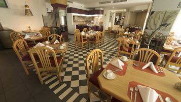 A restaurant with checkered flooring, wooden chairs, and tables set with white napkins and silverware.