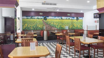 A restaurant with checkered flooring, wooden tables and chairs, and a mural of a field on the back wall.