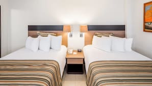 Habitación de hotel con dos camas, cada una con ropa de cama a rayas, una mesita de noche con lámpara y un cuadro en la pared.