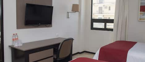 Una habitación de hotel con cama, escritorio, silla, televisor y ventana con cortinas.