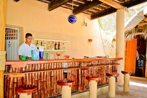 A bar area with a wooden counter, stools, and a shelf with bottles. - Catalina Beach Resort (Zihuatanejo)