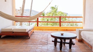 Una habitación con una hamaca, una cama, una mesa redonda y vista al mar.