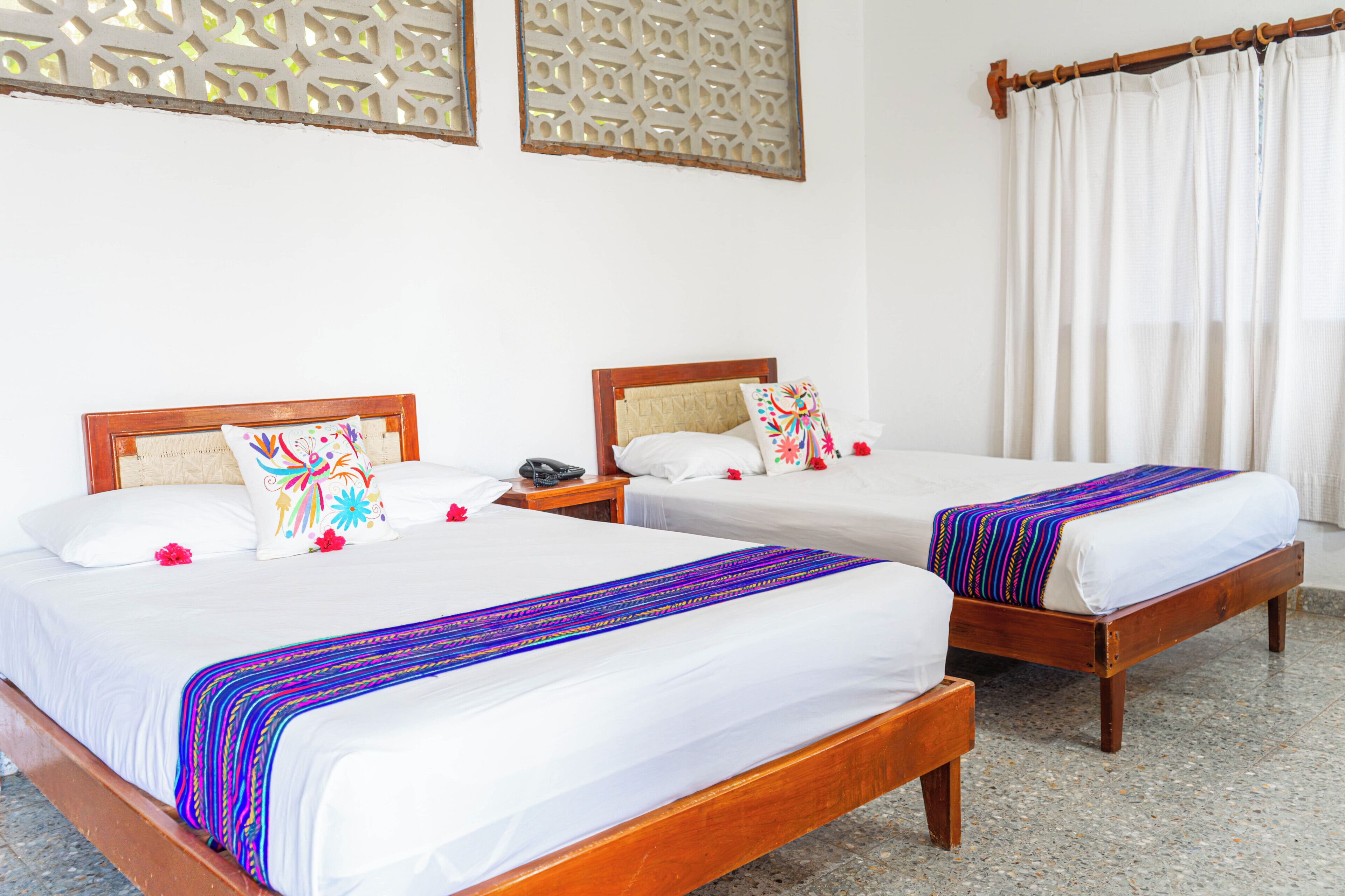 Two wooden beds with white linens, a nightstand with a phone, and a decorative wall panel.