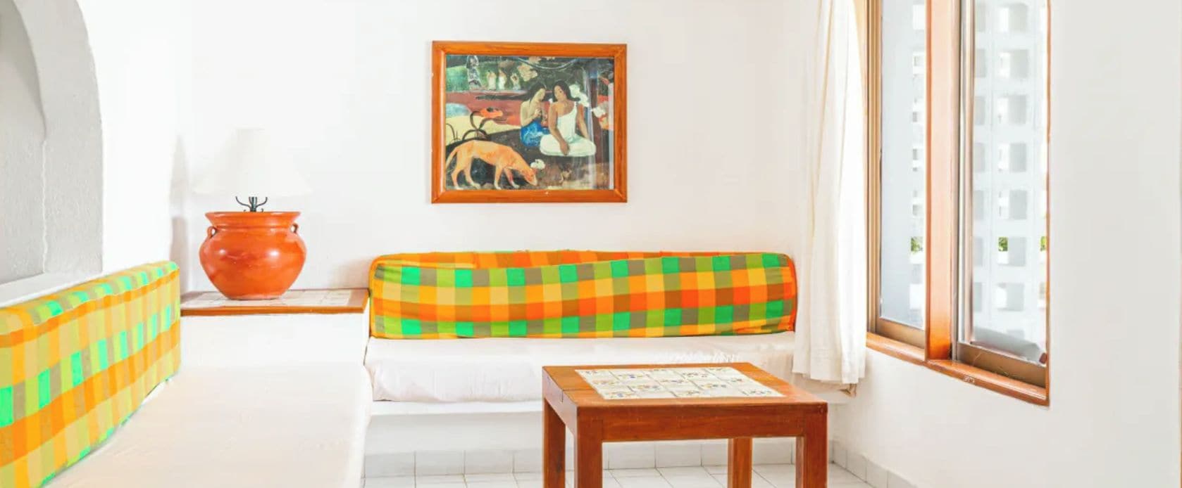 A room with a checkered sofa, a wooden table, a large orange pot, and a painting on the wall.