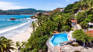 Un hotel frente al mar con piscina, vistas a la playa y vegetación tropical.