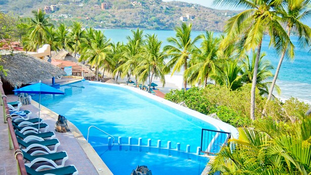 A pool with lounge chairs and a view of the ocean.