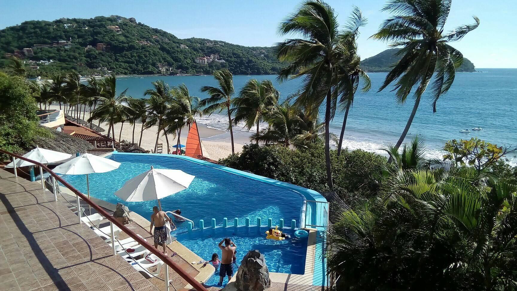A pool area with a view of the beach and ocean, surrounded by palm trees.
