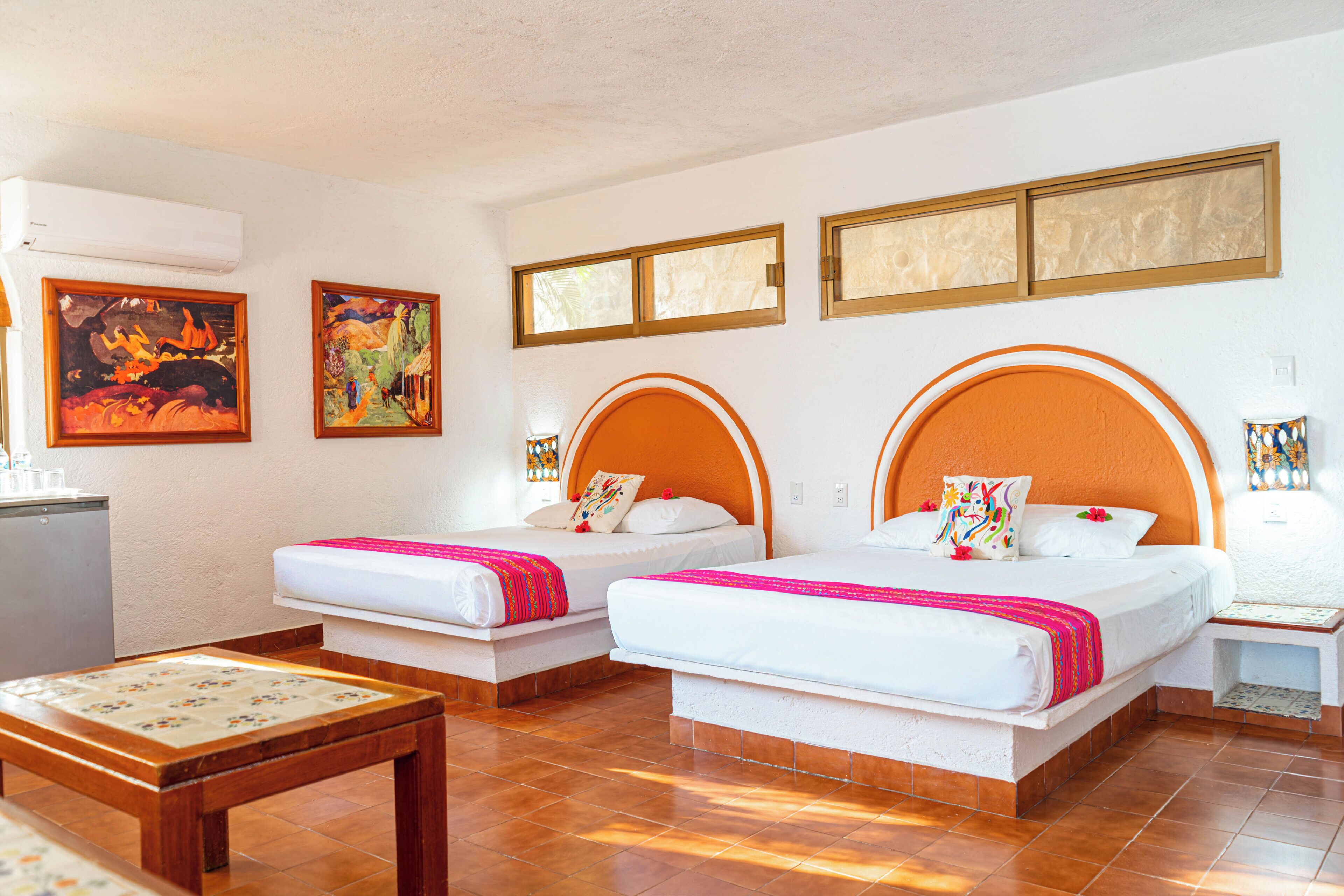 A hotel room with two beds, a small table, and artwork on the walls.