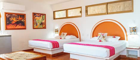 Una habitación de hotel con dos camas, una mesita y obras de arte en las paredes.