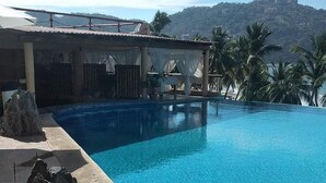 A clear blue infinity pool with a view of a mountain and palm trees in the background.