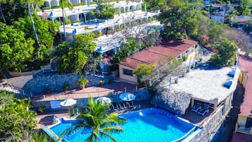 An aerial view of a resort with a swimming pool, multiple buildings, and lush greenery.