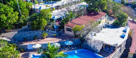 Vista aérea de un complejo turístico con piscina, varias edificaciones y abundante vegetación.