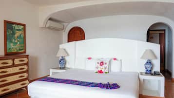 Habitación de hotel con una cama grande, dos mesitas de noche con lámparas, un aparador y un cuadro en la pared, además de un arco de entrada.