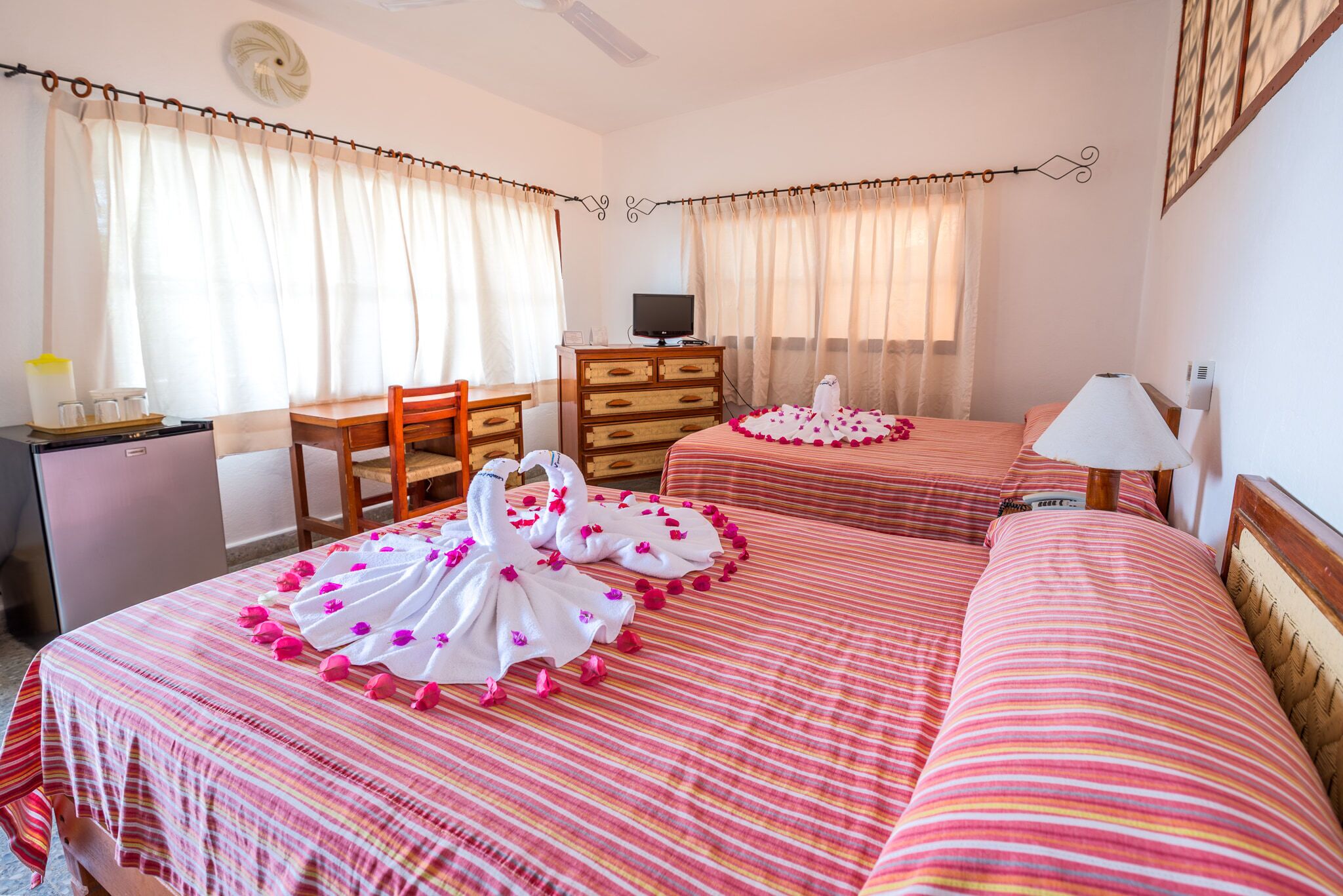 A hotel room with two beds, a desk, a TV, and a dresser.