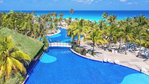 A resort pool with a clear view of the ocean, surrounded by palm trees and lounge chairs. - The Grand Oasis Cancun - All Inclusive (Cancun)