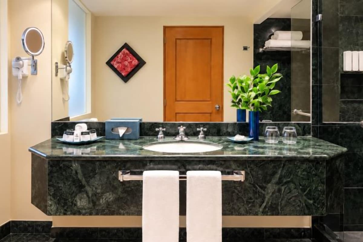 A bathroom with a marble sink, a mirror, a potted plant, and a towel rack.
