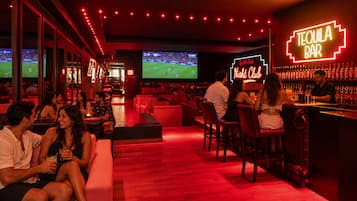 A bar area with a neon sign reading 'TEQUILA BAR' and a large screen displaying a sports event.