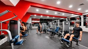 Un gimnasio con diferentes equipos de ejercicio, una decoración en colores rojo y blanco, y un diseño moderno.