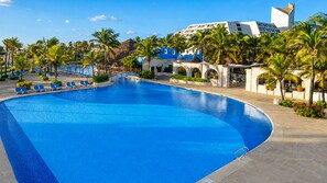 A large swimming pool with blue water, surrounded by palm trees and a building with blue and white architecture. - The Grand Oasis Cancun - All Inclusive (Cancun)