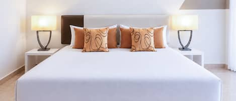Una cama bien tendida con colchón blanco y cabecera marrón, flanqueada por dos mesitas de noche con lámparas, en una habitación de estilo minimalista.