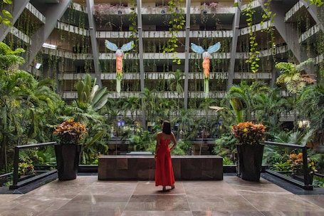 A spacious atrium with a central walkway, surrounded by lush indoor plants and hanging decorations.