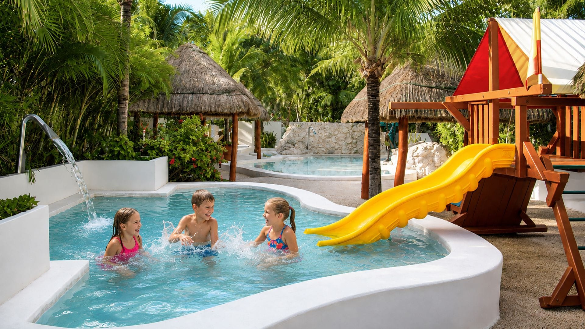 Una piscina con tobogán, rodeada de palmeras y construcciones de techo de paja.