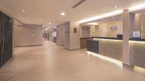 A hotel reception area with a modern design, featuring a reception desk, a sign for Hampton Inn, and a hallway leading to other rooms. - Hampton Inn by Hilton Monterrey/Galerías-Obispado (Monterrey)