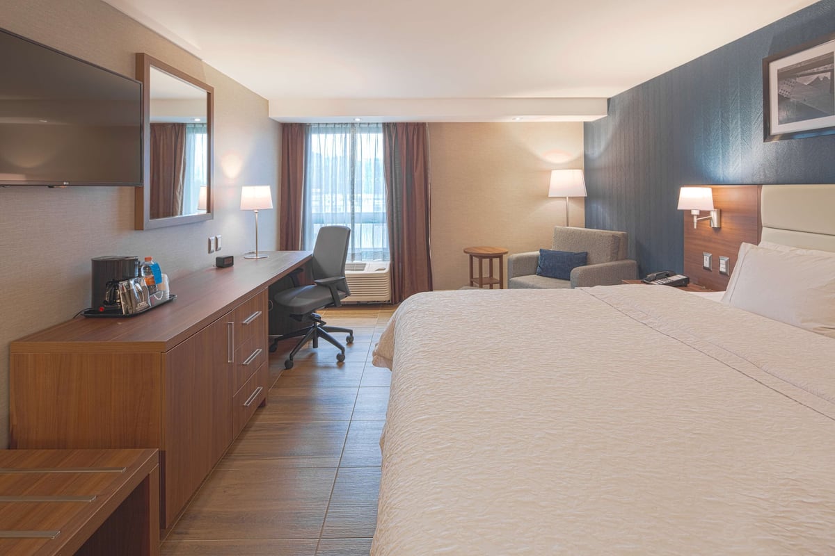 A hotel room with a large bed, a desk with a chair, a small table, and a TV.
