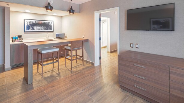 A modern kitchen with a bar area, wooden flooring, and a flat-screen TV mounted on the wall. - Hampton Inn by Hilton Monterrey/Galerías-Obispado (Monterrey)