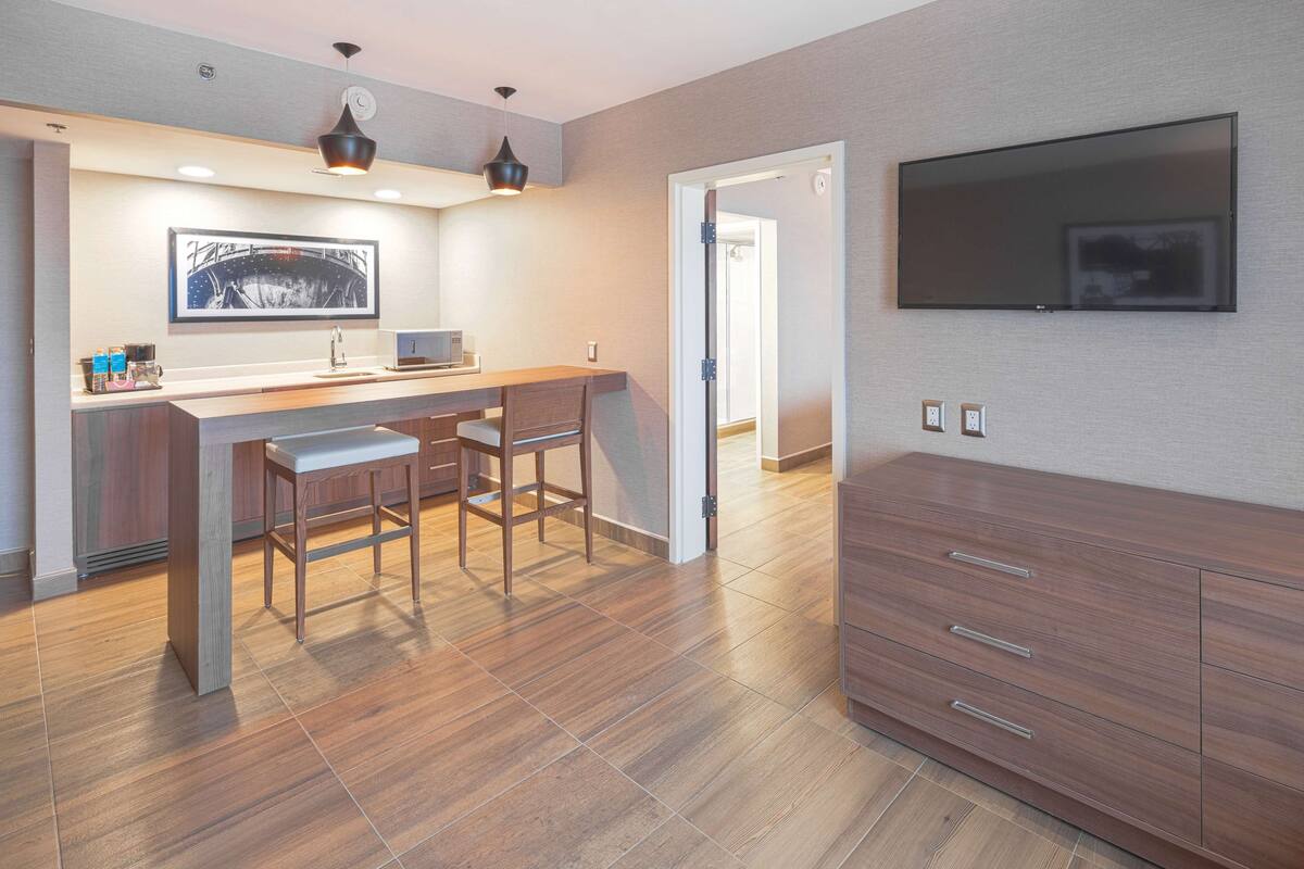 A modern kitchen with a bar area, wooden flooring, and a flat-screen TV mounted on the wall.