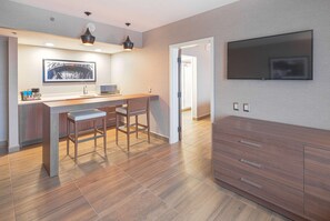A modern kitchen with a bar area, wooden flooring, and a flat-screen TV mounted on the wall. - Hampton Inn by Hilton Monterrey/Galerías-Obispado (Monterrey)