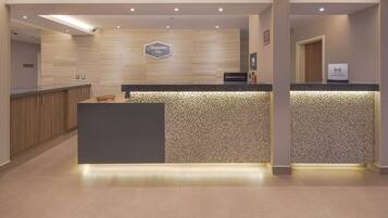 Zona de recepción de un hotel con pared de madera, mostrador de recepción y un cartel que dice "Hampton Inn by Hilton".